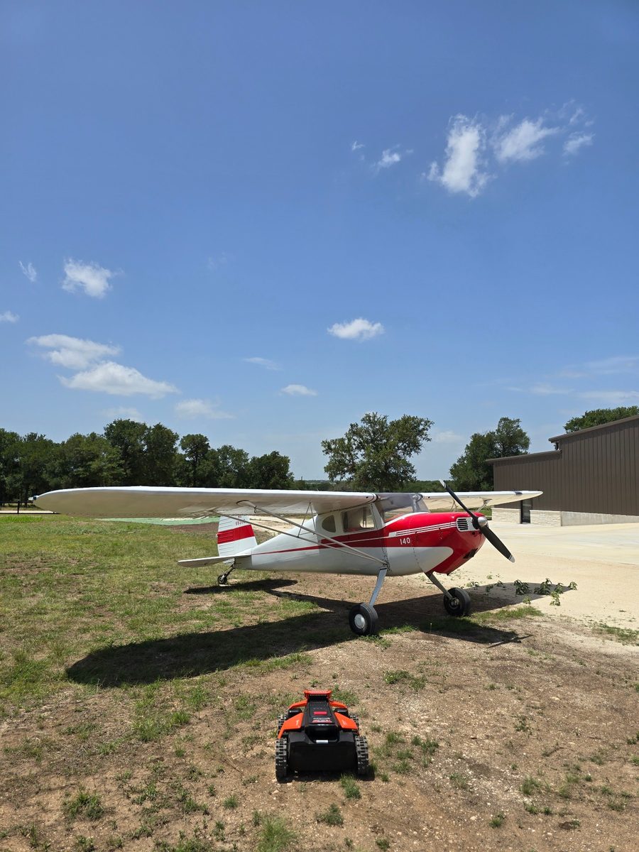 A taildragger parked on the ramp at a Bertram flight school, mower working the turf alongside